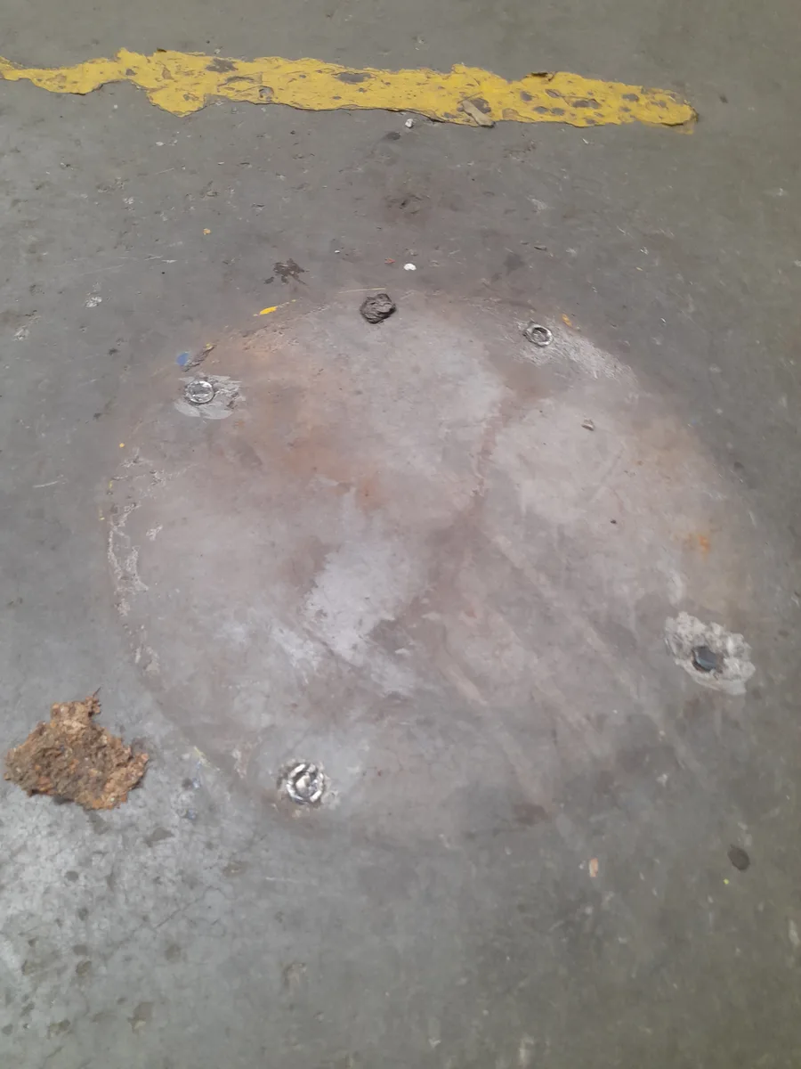 Multiple exposed anchor bolts across machine base footprint on warehouse floor before reinstatement — Christchurch