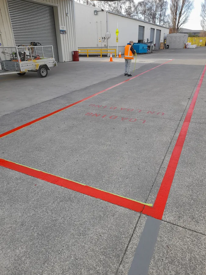 Red boundary line marking on outdoor loading zone with hi-vis worker